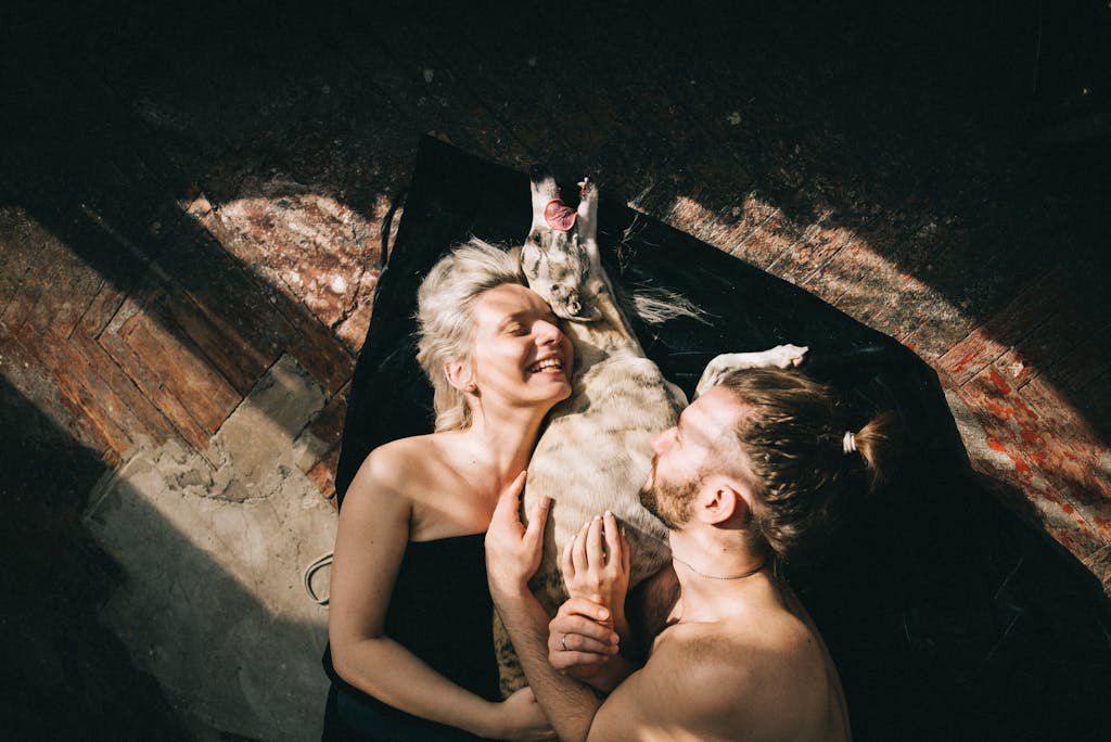 A happy couple and their dog enjoying a moment of affection and joy on the floor indoors.