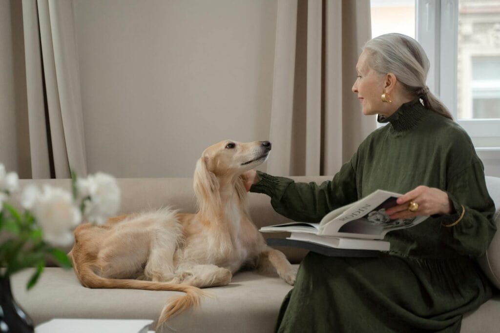 Elegant senior woman reading with a Saluki dog on a living room sofa.