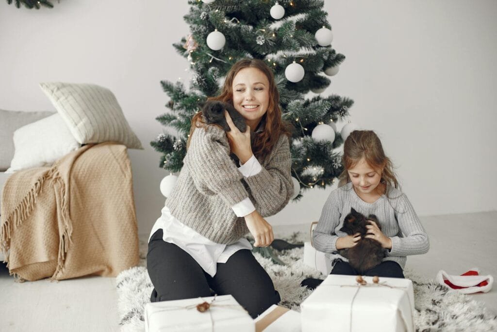 A mother and daughter enjoy playful moments with kittens by the Christmas tree.
