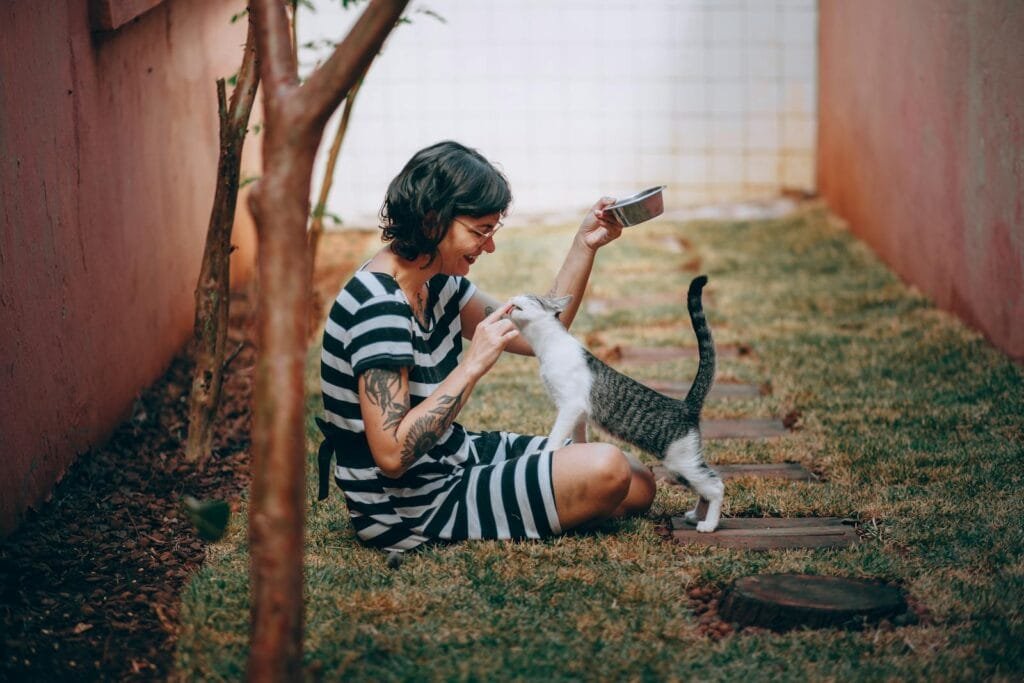 Woman playing with her cat outdoors in a garden, showcasing a joyful moment.