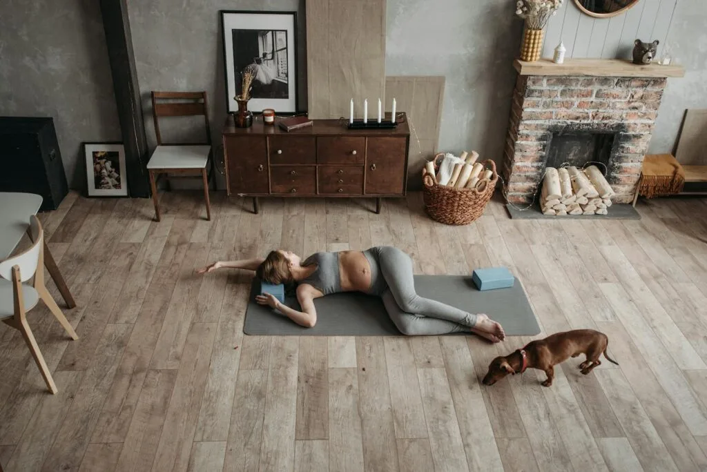 Pregnant woman doing yoga with her dachshund dog in cozy home environment, fostering relaxation.